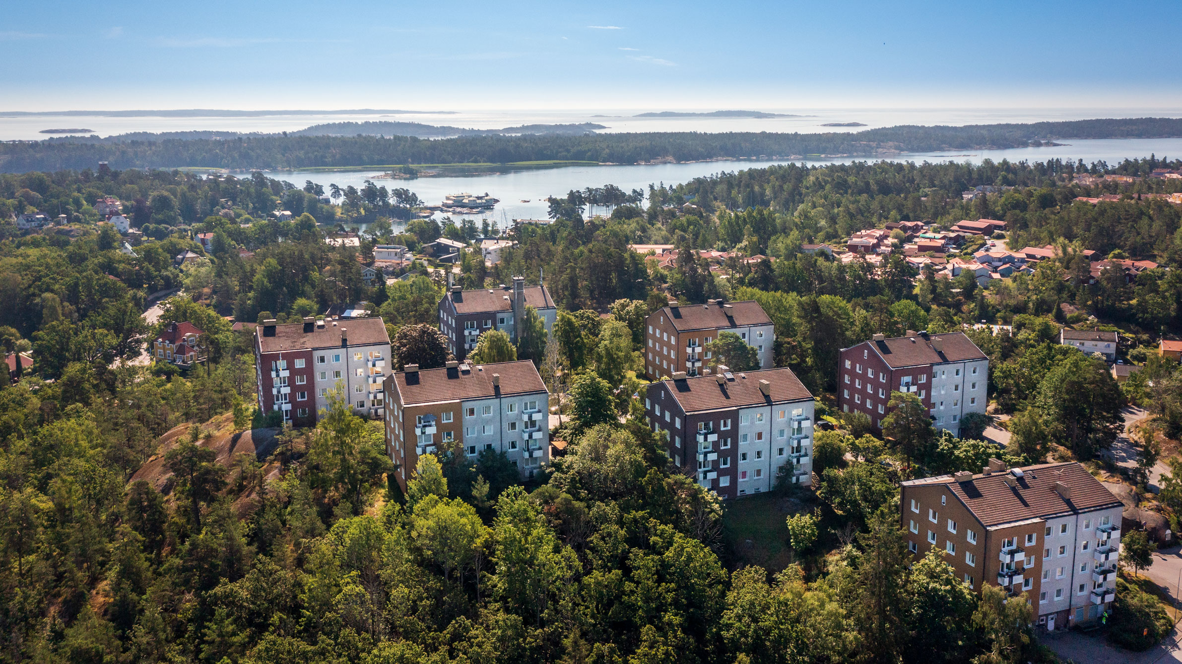 Flera flerfamiljshus omgivna av frodig grönska längs Toppstigen i Nynäshamn. I bakgrunden syns skärgården med vatten och små öar som sträcker sig mot horisonten.