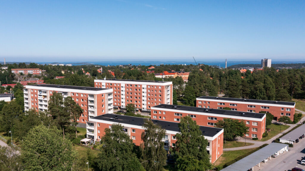 Flerbostadshus på Backluravägen 3 till 11, Nynäshamn, med vy över omgivningen och havet i bakgrunden. Byggnaderna är omgivna av grönska och träd, vilket bidrar till en lugn och naturskön atmosfär.