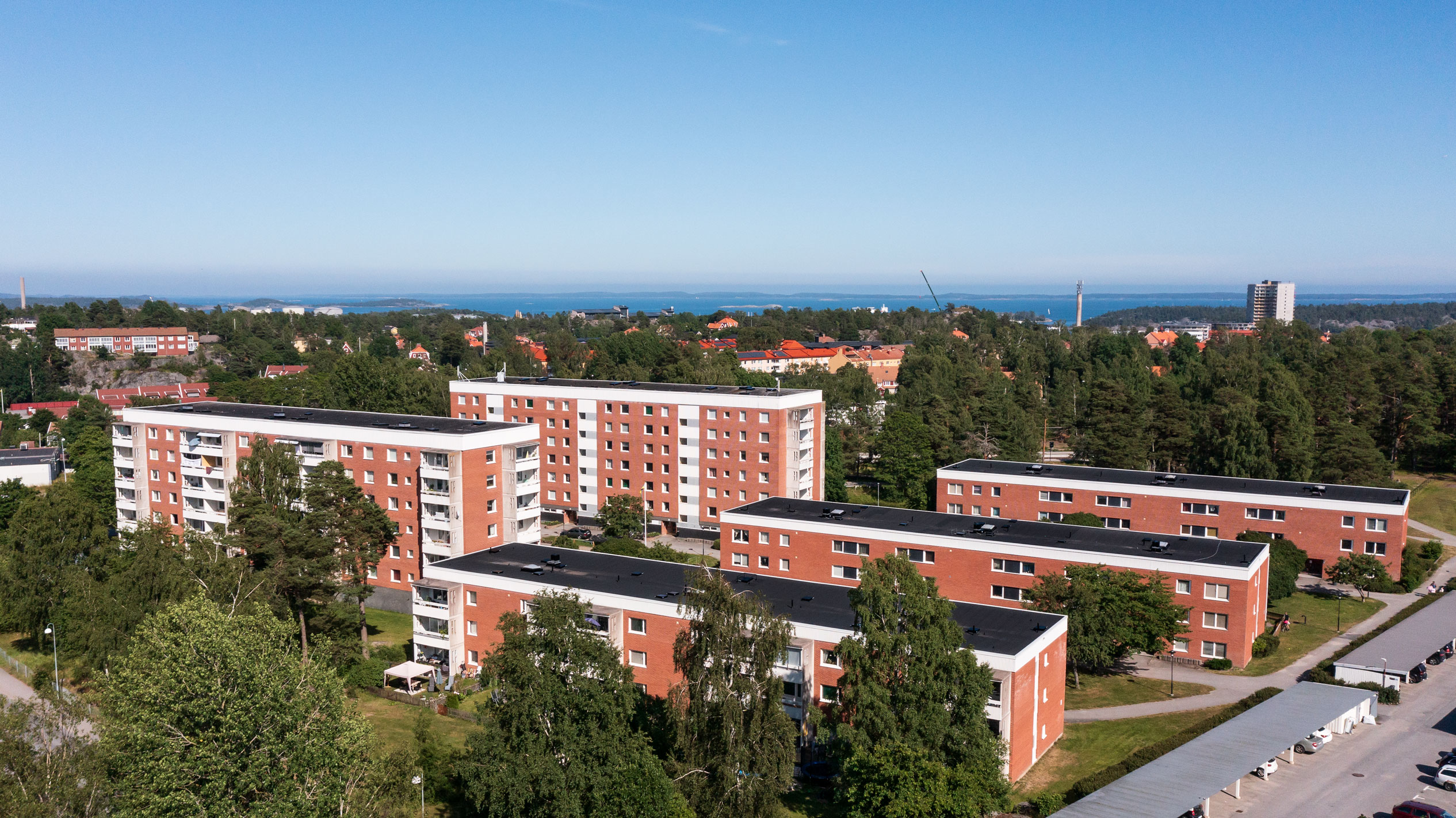 Flerbostadshus på Backluravägen 3 till 11, Nynäshamn, med vy över omgivningen och havet i bakgrunden. Byggnaderna är omgivna av grönska och träd, vilket bidrar till en lugn och naturskön atmosfär.