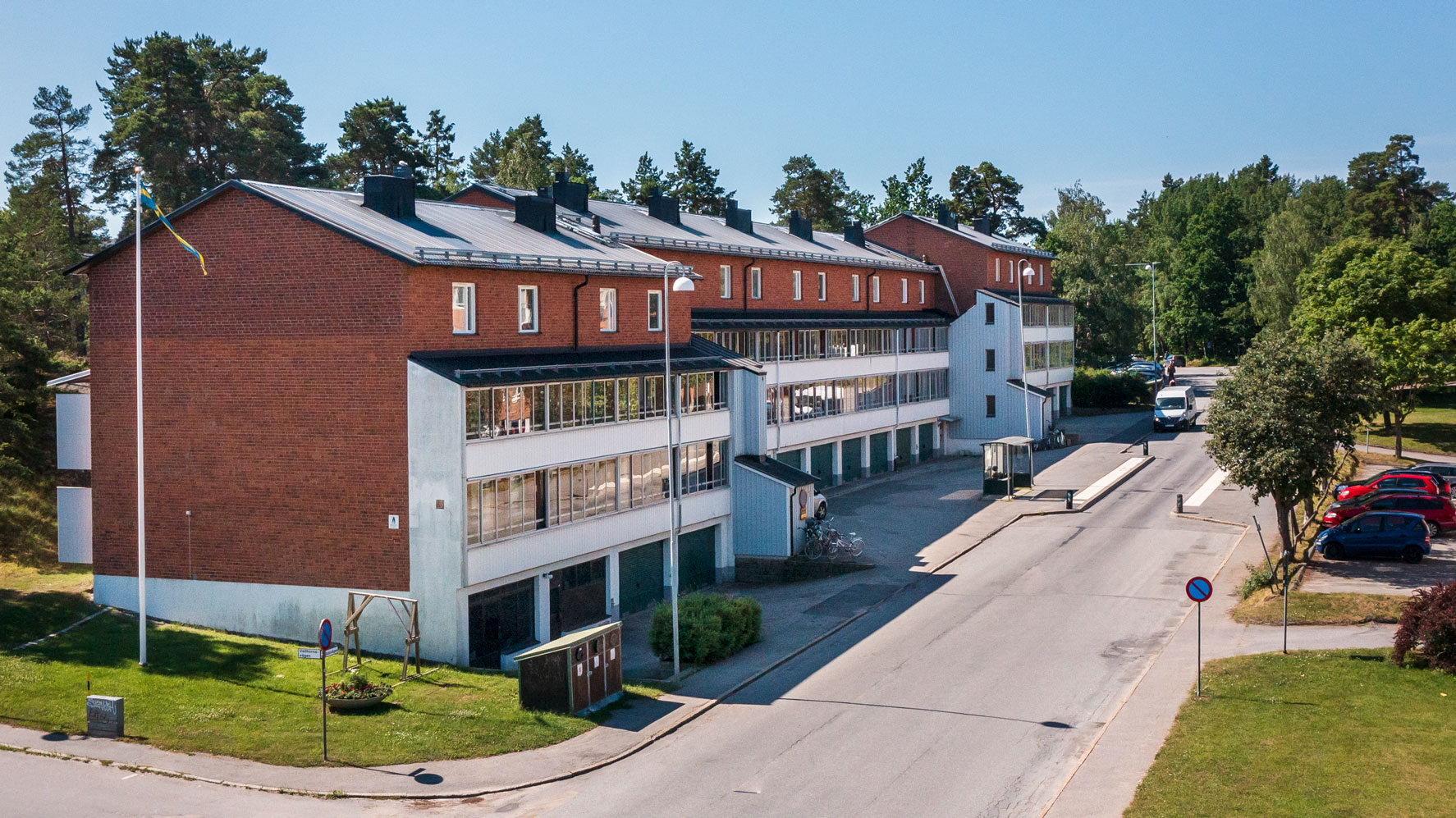 Hyreslägenheter på Estövägen 5 A och B i Nynäshamn, med röda tegelbyggnader och balkonger, omgivna av träd och grönska. Perfekta hyreslägenheter i en naturskön miljö.